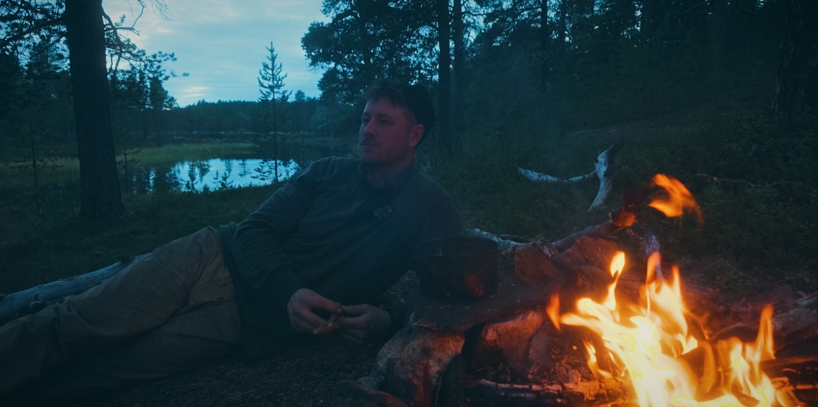 Sakke Raappana lepää iltanuotion ääressä järven rannalla Lapissa