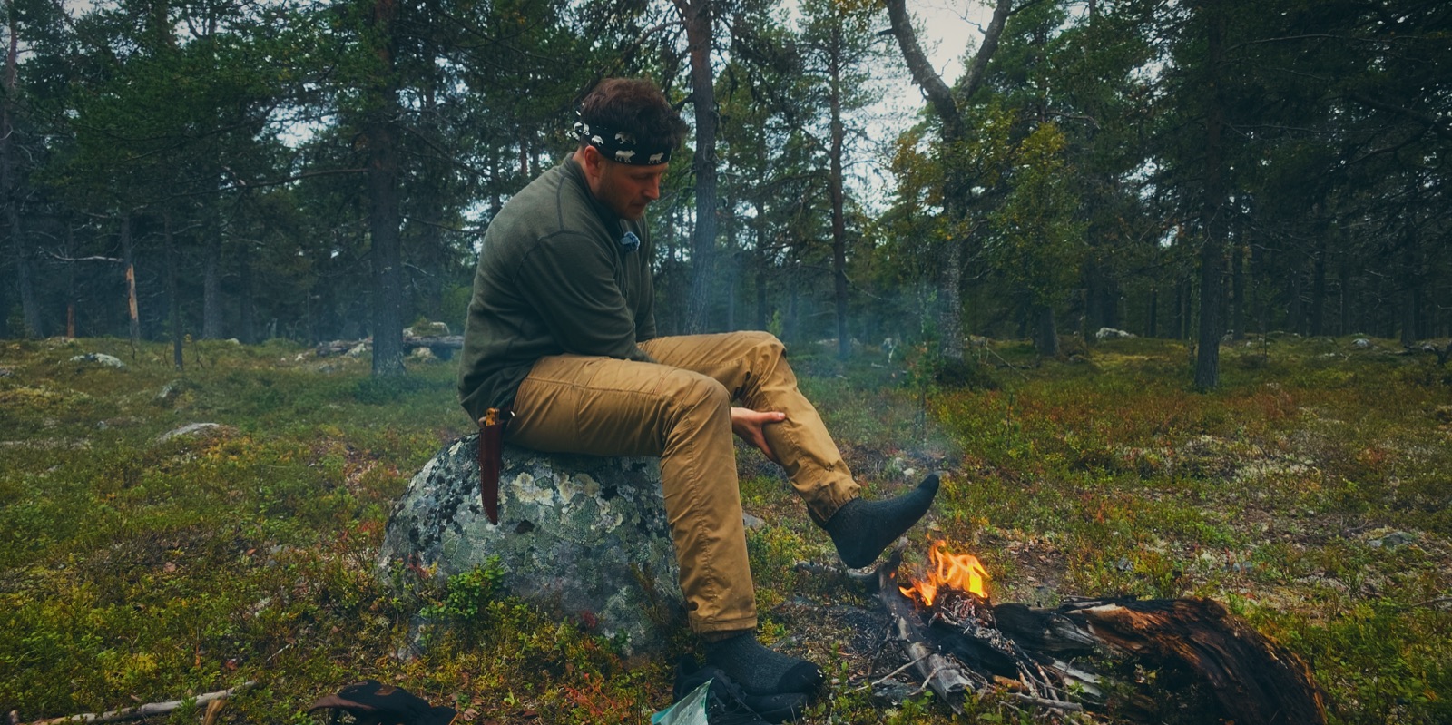 Sakke Raappana istuu kivellä nuotion vieressä mäntymetsässä Lapissa